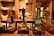 A row of traditional beer taps is lined up on a wooden bar inside a cozy pub setting, with various types of beer and ale bottles displayed on shelves in the background. Warm lighting creates a rustic and inviting atmosphere.