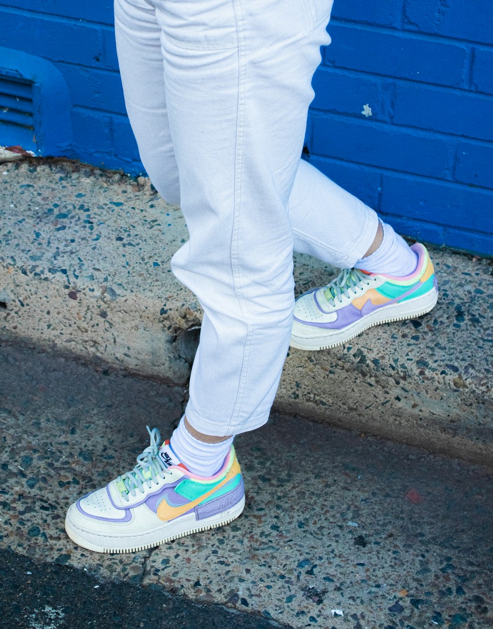 person in blue denim jeans and white green and pink nike sneakers