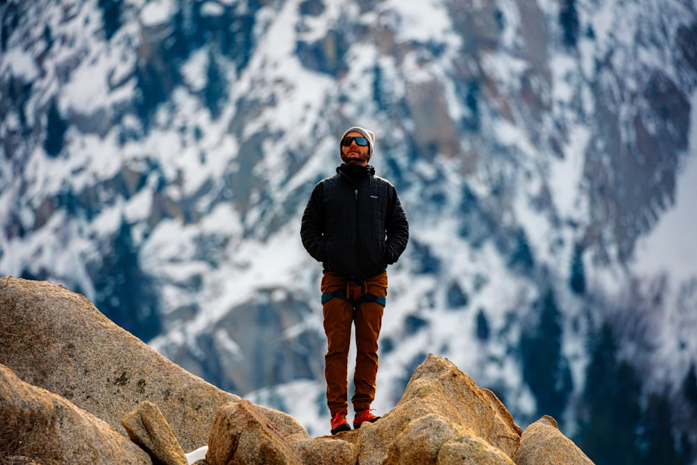 man in black jacket and brown pants standing on brown rock formation during daytime