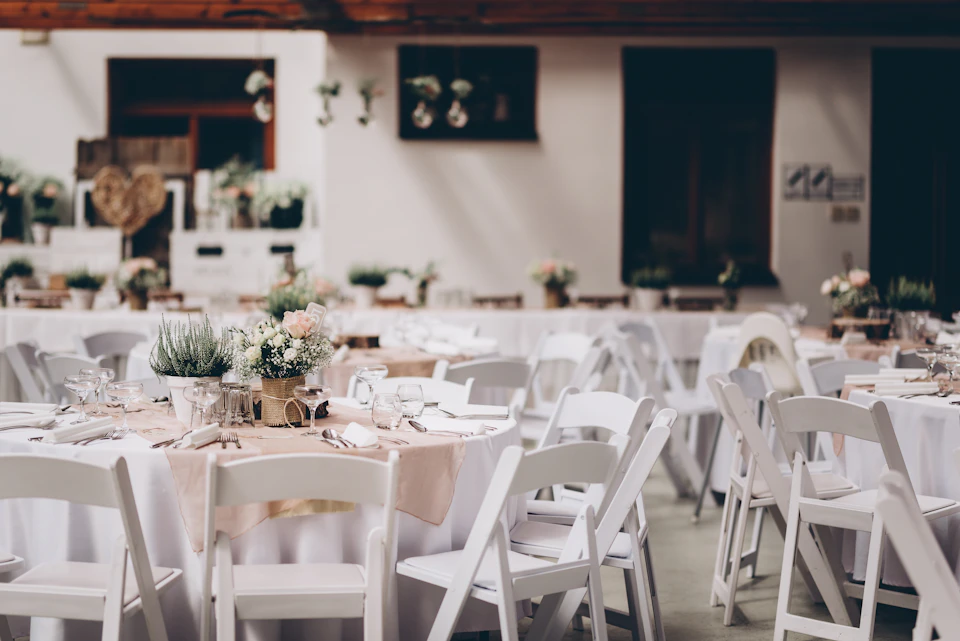 A reception hall set with round tables, white chairs and small flower arrangements before guests arrive