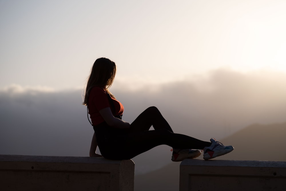 woman in red tank top and black pants sitting on concrete bench during daytime