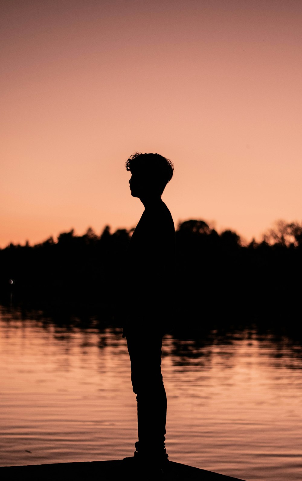 silhouette of woman standing on water during sunset