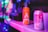 A vibrant scene featuring an orange can of Ace Hill Kombucha prominently placed on a shelf. The background includes various unfocused objects with colorful, blurred lights creating a lively atmosphere. Another can, partially blurred, is visible to the right.