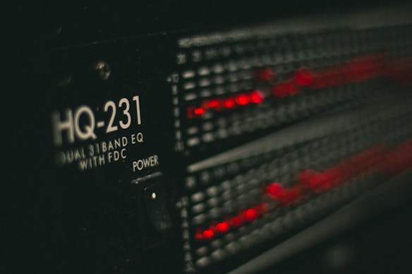 A close-up of a piece of audio equipment, specifically an equalizer labeled HQ-231 with glowing red LED indicators. The surrounding area is dark, focusing attention on the illuminated details of the device.