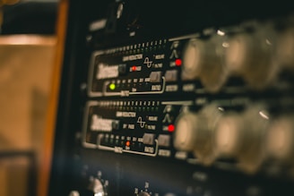 A close-up view of electronic audio equipment, likely a rack-mounted audio compressor or processor, showing control knobs, LED indicators, and markings for various settings and functions.