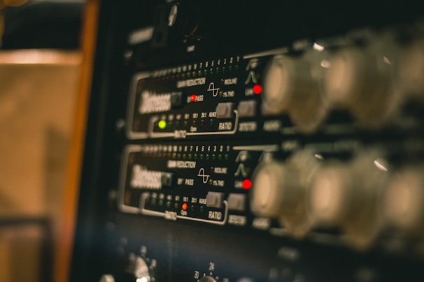 A close-up view of electronic audio equipment, likely a rack-mounted audio compressor or processor, showing control knobs, LED indicators, and markings for various settings and functions.
