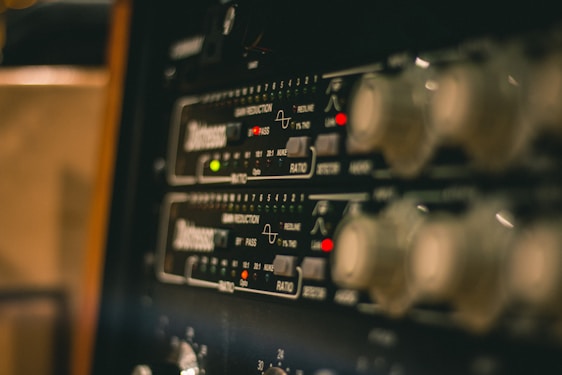 A close-up view of electronic audio equipment, likely a rack-mounted audio compressor or processor, showing control knobs, LED indicators, and markings for various settings and functions.