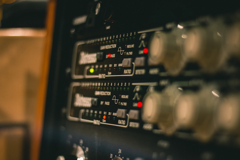 A close-up view of electronic audio equipment, likely a rack-mounted audio compressor or processor, showing control knobs, LED indicators, and markings for various settings and functions.