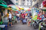 A sunlit street market in Southeast Asia bustling with colorful stalls and local vendors.