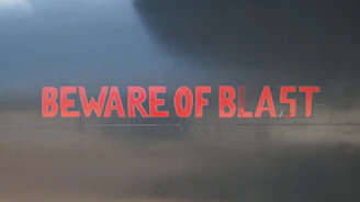 A stark red warning sign with bold text 'Beware Greg Secker Schemes' against a clean white background.