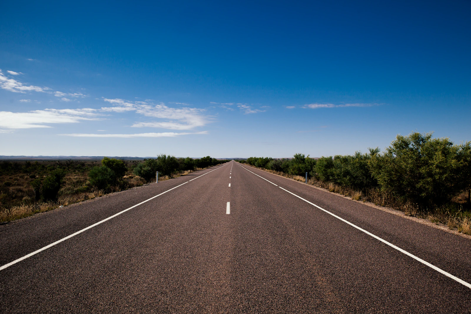 An empty Australian highway runs beneath a clear blue sky