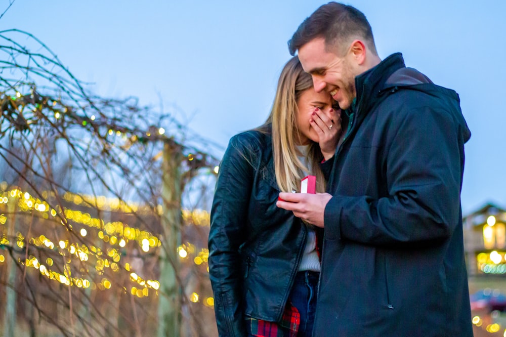 man in black jacket kissing woman in black jacket during daytime