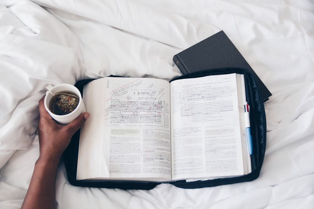 person holding white ceramic mug on white book page