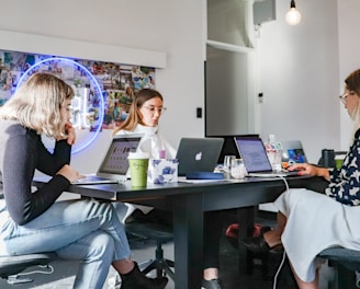 3 women sitting on chair in front of table with laptop computers