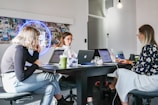 3 women sitting on chair in front of table with laptop computers