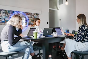 3 women sitting on chair in front of table with laptop computers