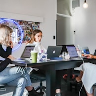 3 women sitting on chair in front of table with laptop computers