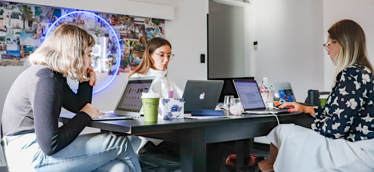 3 women sitting on chair in front of table with laptop computers