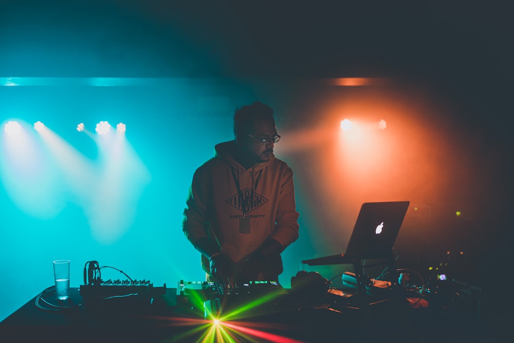 man in brown hoodie standing in front of macbook pro