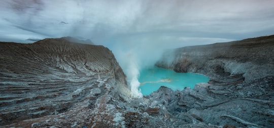 brown rocky mountain near body of water under white clouds during daytime in Ijen Indonesia