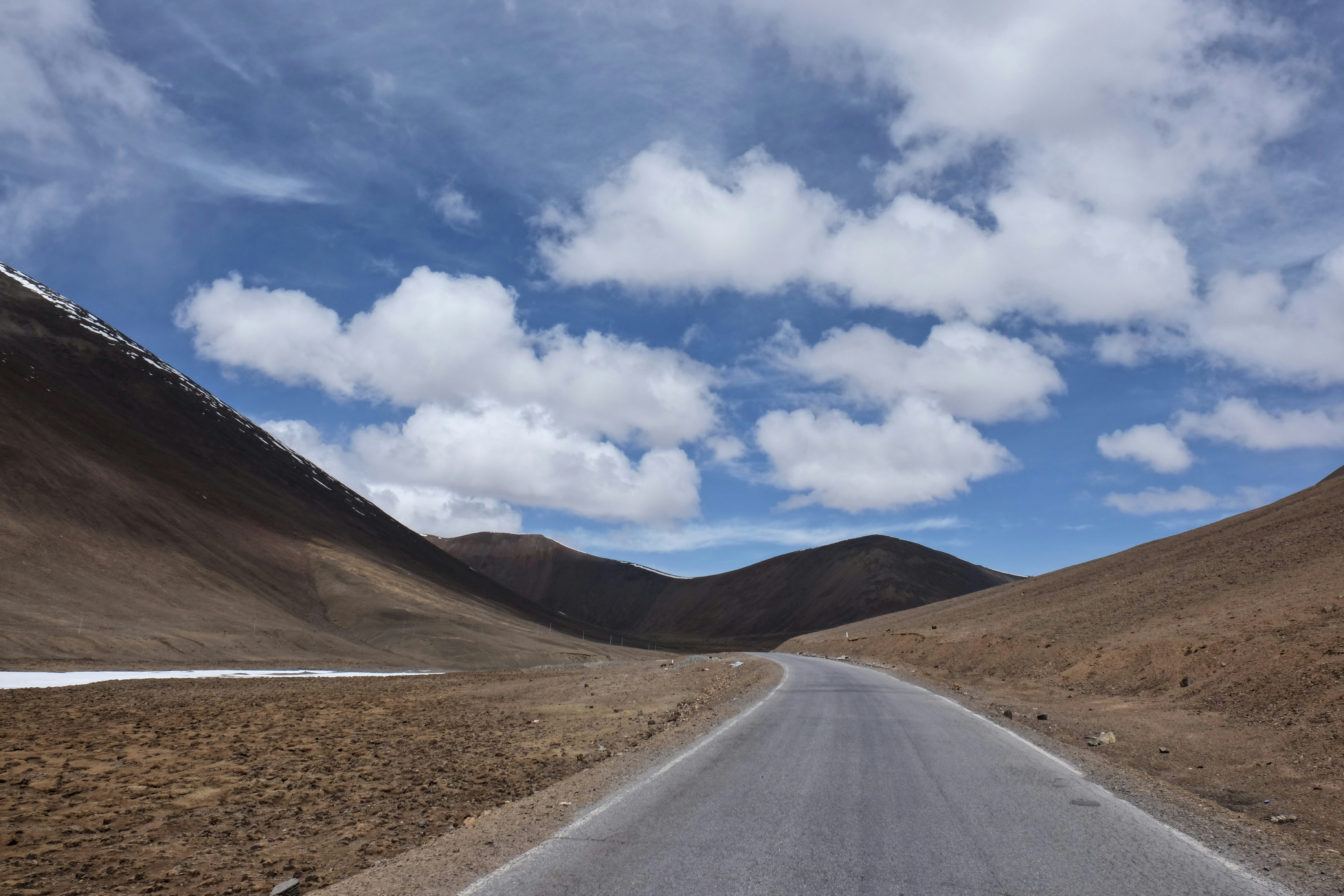 gray asphalt road under blue sky and white clouds during daytime