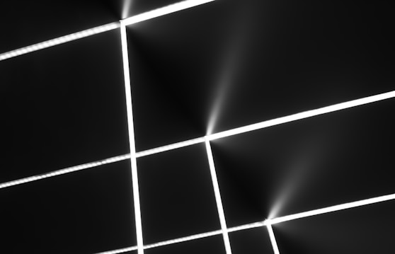 Intersecting white lines create a grid pattern against a dark background. The lines are bright and emit a slight glow, suggesting a futuristic or digital theme. The overall composition is minimalistic and geometric.