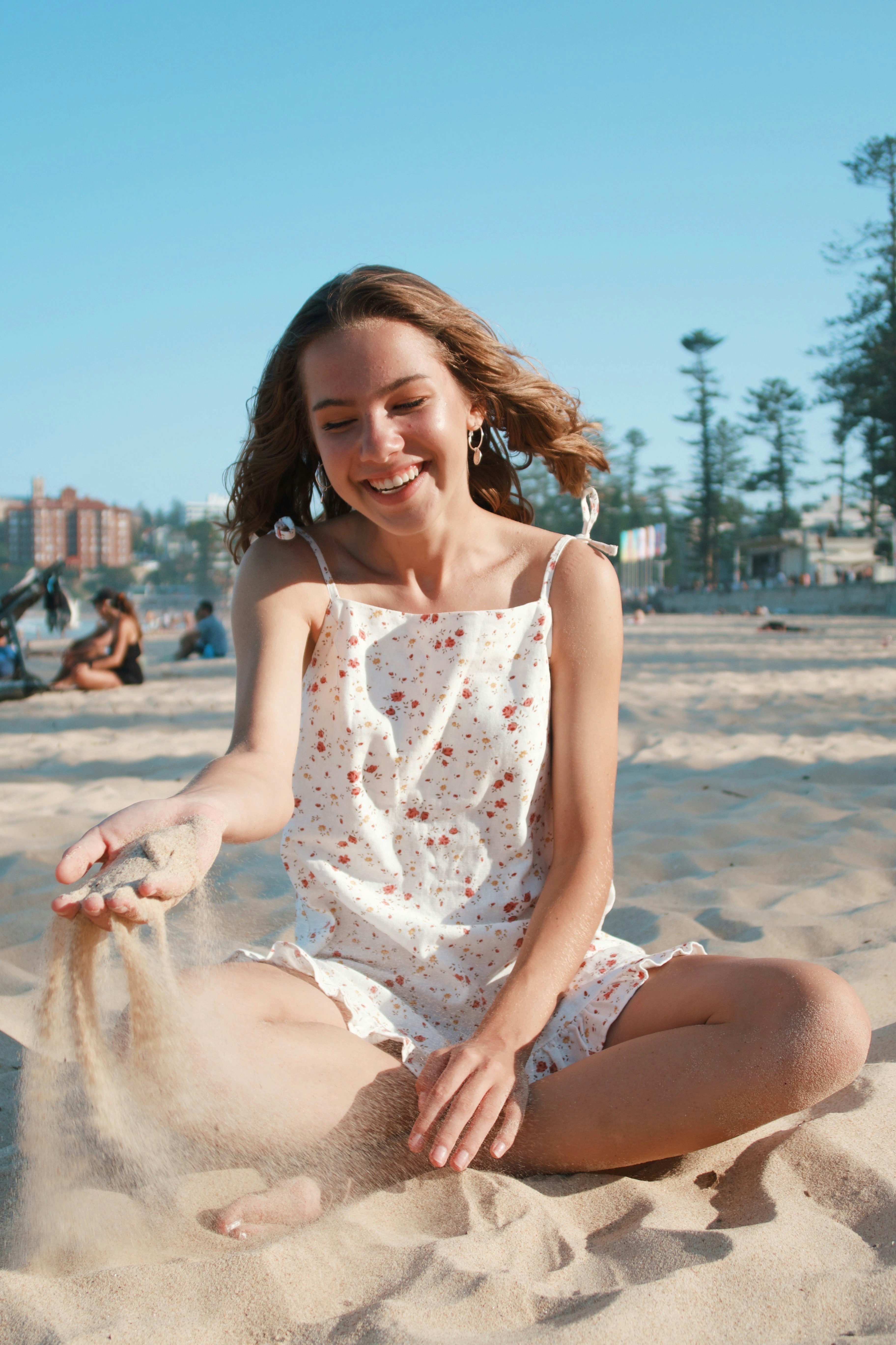 woman in white floral spaghetti strap dress sitting on brown sand during daytime