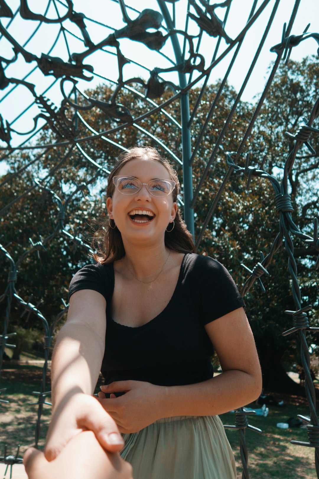 smiling woman in black scoop neck t-shirt standing near green plants during daytime