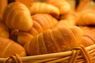 A basket full of freshly baked croissants with a golden-brown crust and flaky texture. The image highlights the warm and inviting look of the pastries, arranged closely together.