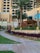 A luxurious hotel exterior featuring a multi-story classical architectural design with large windows and ornate details. Tall palm trees are planted around a beautifully landscaped garden with pathways. A restaurant sign named 'Miss India' is visible, and ambient lighting enhances the elegant setting.