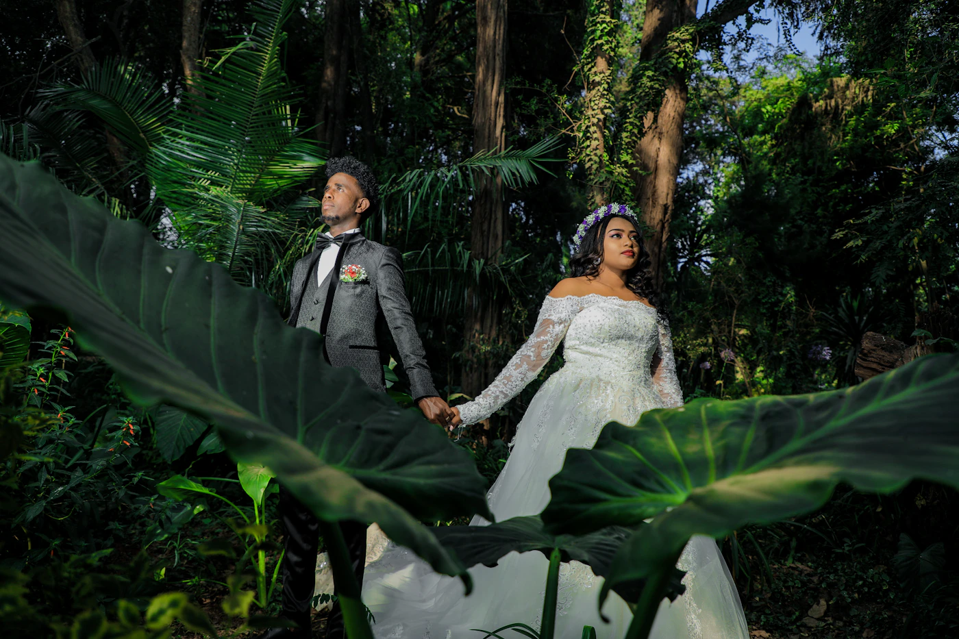 Couple in ceremony attire on a riverbank in the Ecuadorian Amazon basin with the primary forest and the jungle canopy visible on the far bank