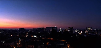 An evening city skyline glowing under the sunset with lights beginning to twinkle.