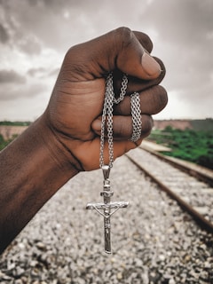 A hand holding a small, worn Thor’s hammer pendant against a backdrop of stormy skies.