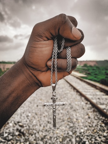 A hand holding a small, worn Thor’s hammer pendant against a backdrop of stormy skies.