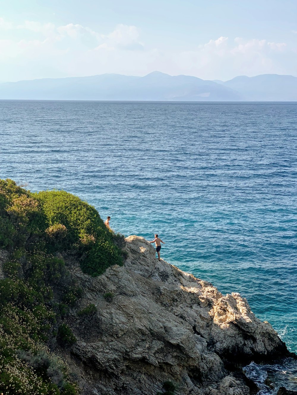 person sitting on rock formation near body of water during daytime