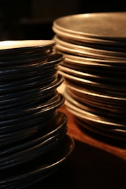 Stacks of metallic plates are arranged closely together, with warm lighting casting highlights and shadows across their surfaces.