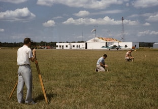 A professional surveyor using a theodolite in a green field under a clear sky