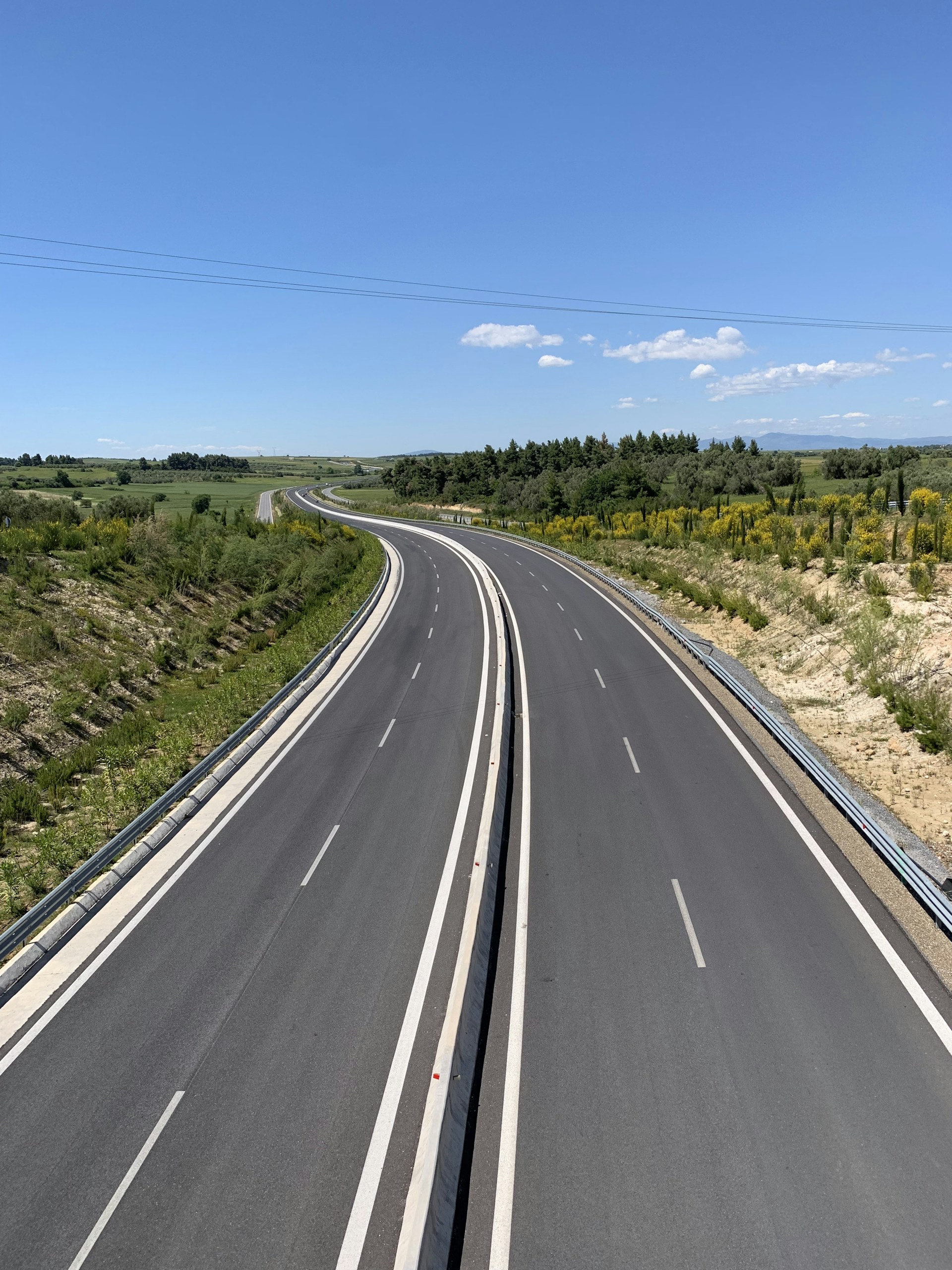 gray asphalt road between green grass field under blue sky during daytime