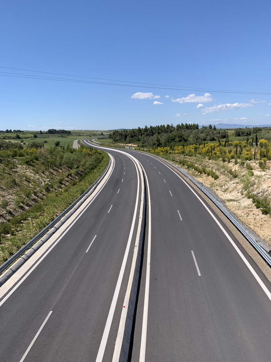 gray asphalt road between green grass field under blue sky during daytime
