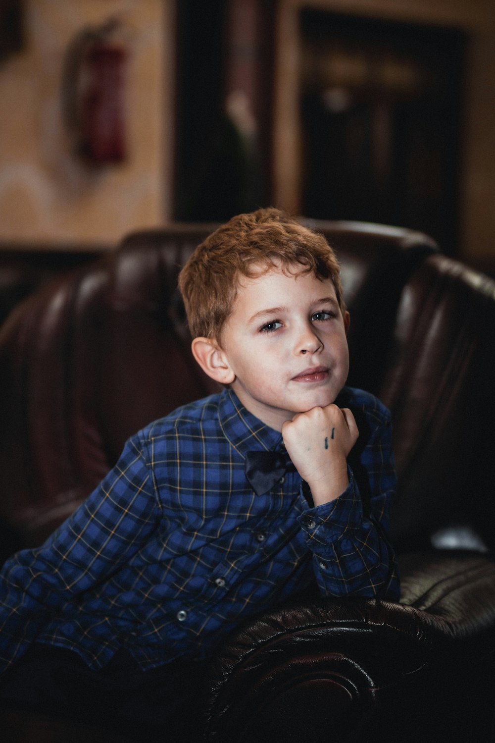 boy in blue and white plaid dress shirt sitting on black leather chair