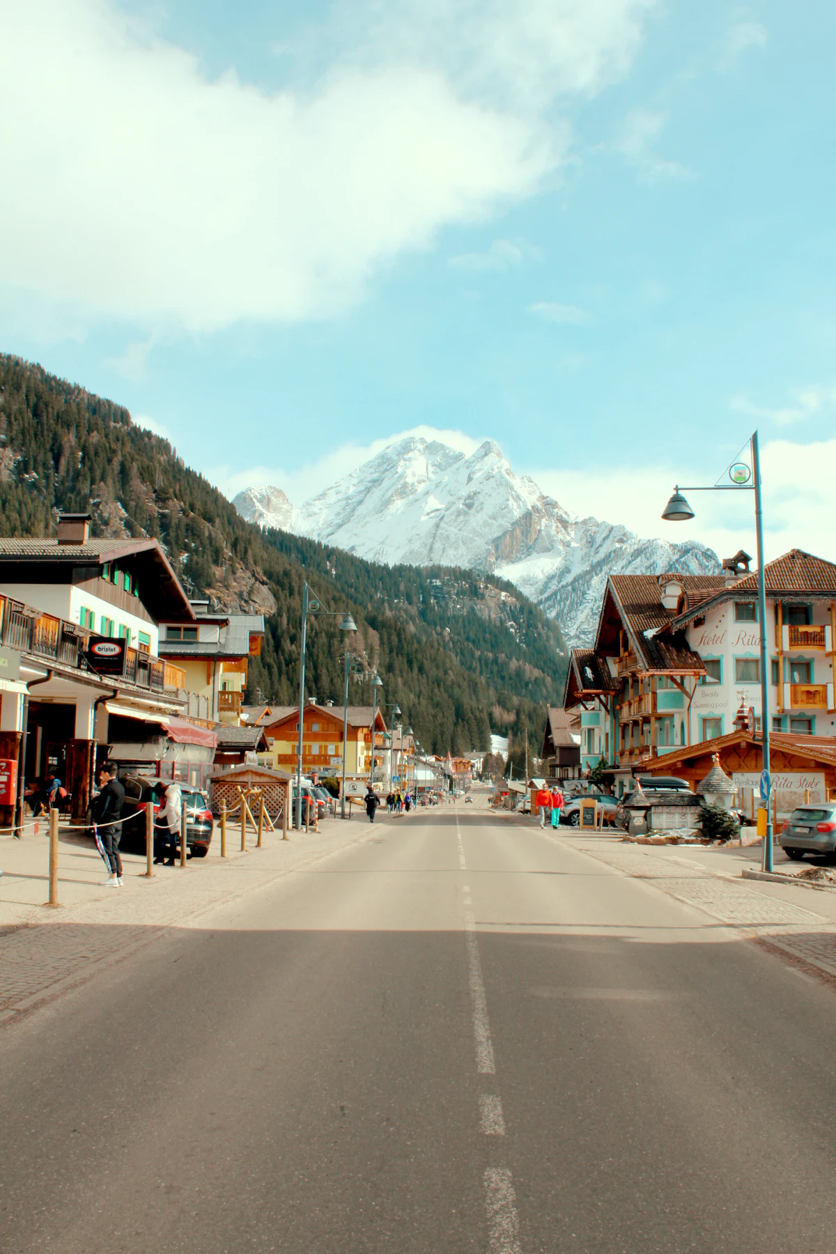 Canazei's main street with shops and hotels, and a snowy peak at the end of the valley