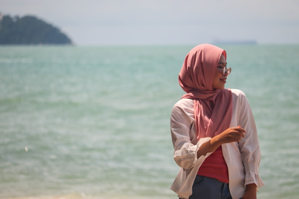 Frau in weißem Langarmhemd und rosa Hijab steht tagsüber in der Nähe des Gewässers