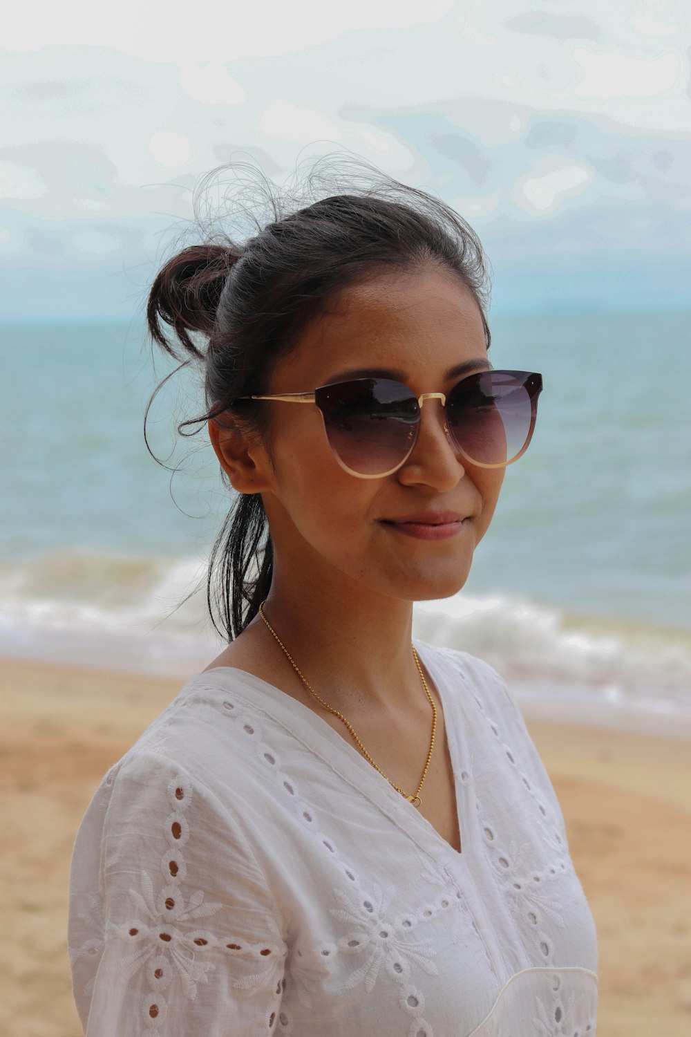 woman in white shirt wearing sunglasses standing on beach during daytime