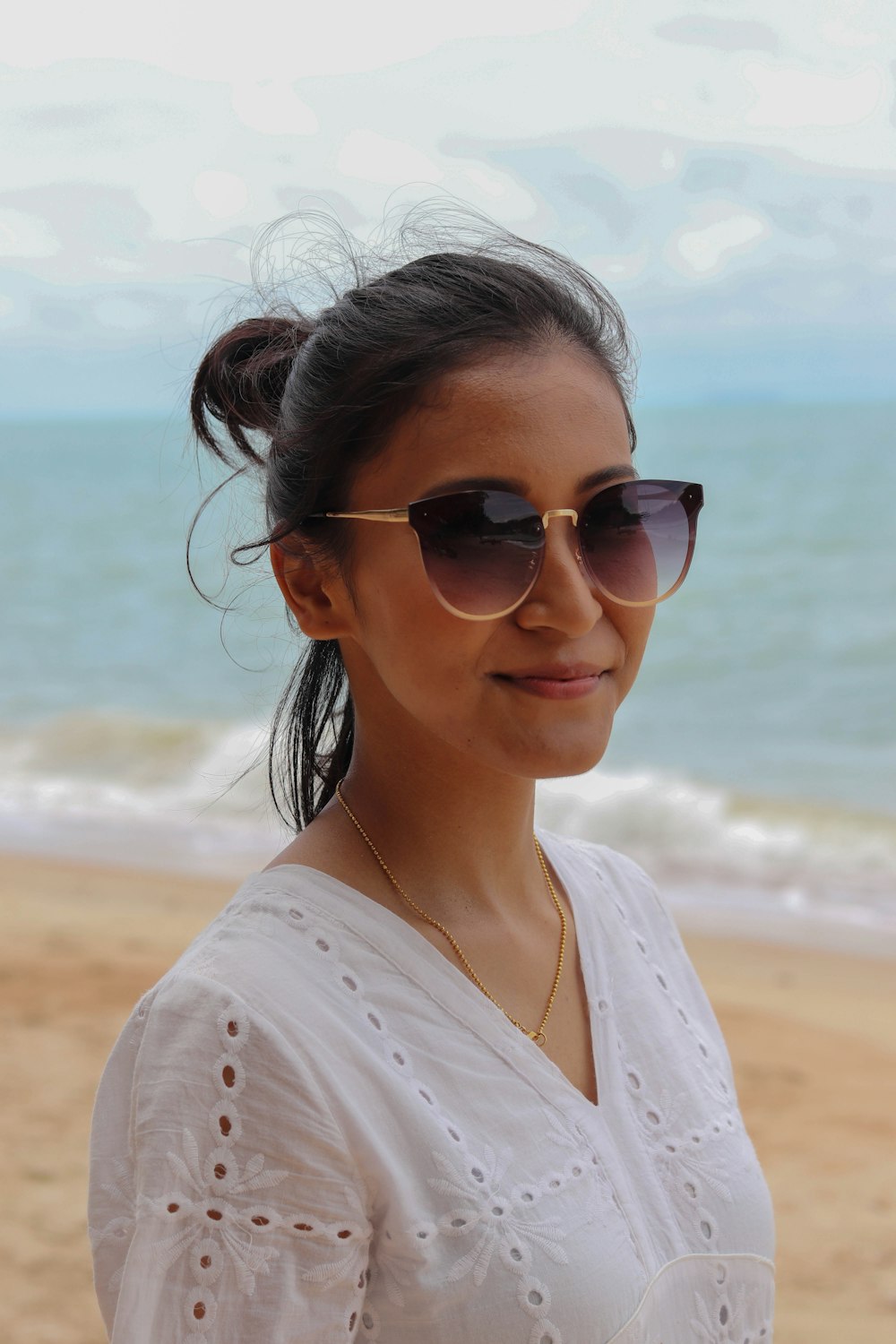 mulher na camisa branca que veste óculos de sol em pé na praia durante o dia