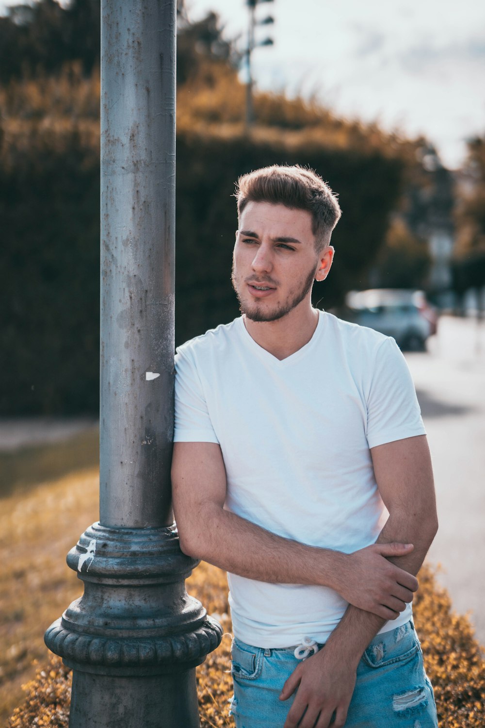 man in white crew neck t-shirt standing beside brown post during daytime