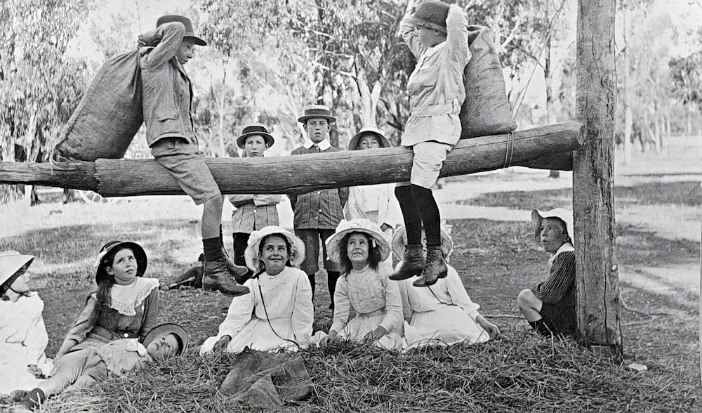 grayscale photo of 2 women and 2 men sitting on wooden fence