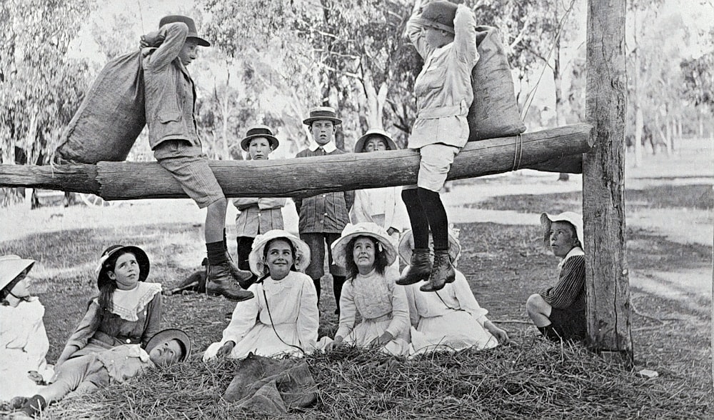 Photo en niveaux de gris de 2 femmes et 2 hommes assis sur une clôture en bois