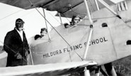 grayscale photo of man in black jacket and pants riding on a plane