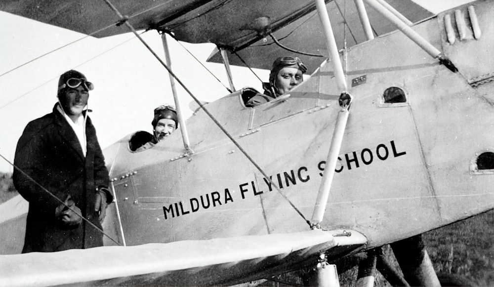 grayscale photo of man in black jacket and pants riding on a plane