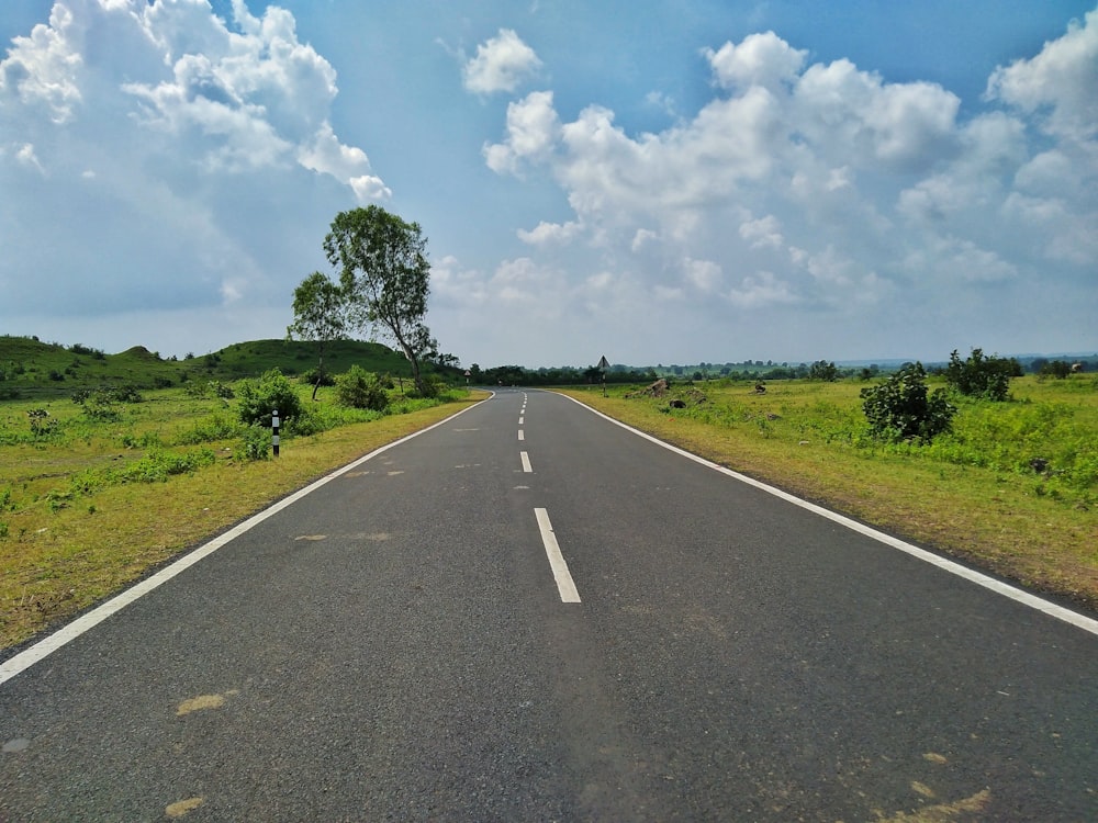 gray concrete road between green grass field under white clouds and blue sky during daytime